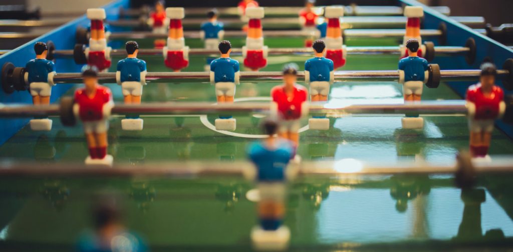 Ein Tischkicker mit roten und blauen Spielfiguren, bereit für ein Spiel, aufgenommen aus der Perspektive eines Spielers.